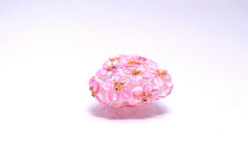 May include: A pink heart-shaped charm made of glass beads, with a design of small pink flowers with gold centers.