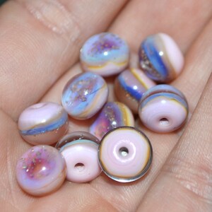 May include: A collection of 10 small, round, glass beads in shades of pink, purple, and blue with iridescent glitter. The beads have a layered, marbled effect.