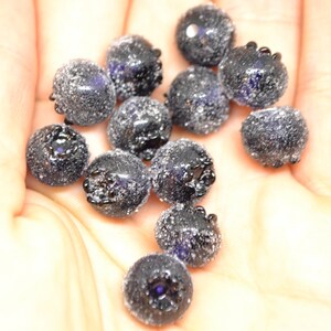 May include: A close-up of a hand holding a pile of dark blue glass beads. The beads are round and have a textured surface.