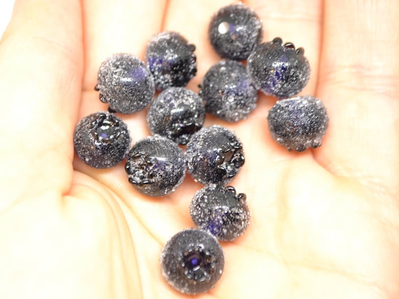 May include: A close-up of a hand holding a pile of dark blue glass beads. The beads are round and have a textured surface.