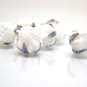May include: Five white glass beads with iridescent blue and purple accents. The beads are round and have a textured surface.
