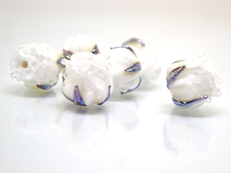 May include: Five white glass beads with iridescent blue and purple accents. The beads are round and have a textured surface.