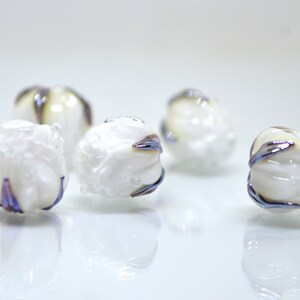 May include: Five white glass beads with iridescent blue and purple accents. The beads are round and have a textured surface.