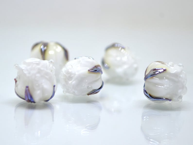 May include: Five white glass beads with iridescent blue and purple accents. The beads are round and have a textured surface.