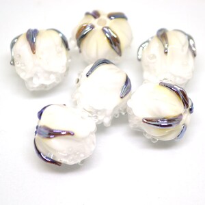 May include: Six white glass beads with iridescent blue and brown accents. The beads are round and have a textured surface.