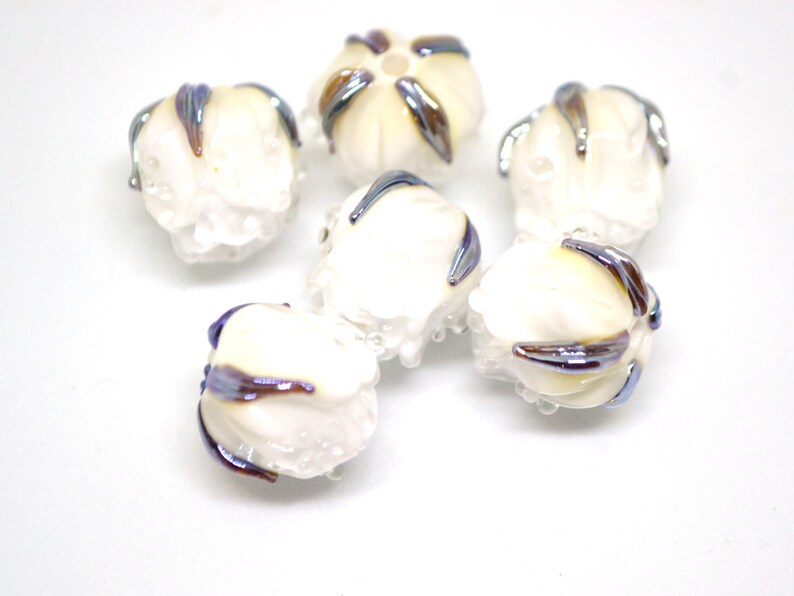 May include: Six white glass beads with iridescent blue and brown accents. The beads are round and have a textured surface.
