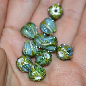 K&ouml;nnte beinhalten: Eine Sammlung gr&uuml;ner und blauer Glasperlen mit aufwendigen Designs. Die Perlen sind blumenf&ouml;rmig und haben eine gl&auml;nzende Oberfl&auml;che.