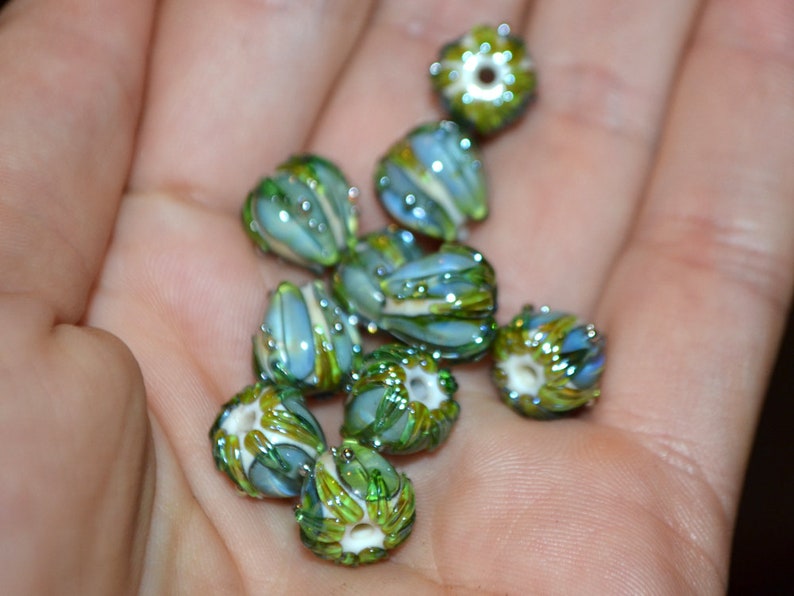 K&ouml;nnte beinhalten: Eine Sammlung gr&uuml;ner und blauer Glasperlen mit aufwendigen Designs. Die Perlen sind blumenf&ouml;rmig und haben eine gl&auml;nzende Oberfl&auml;che.