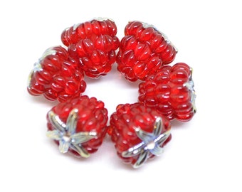May include: Six red glass raspberry beads with silver accents. The beads are arranged in a circle.
