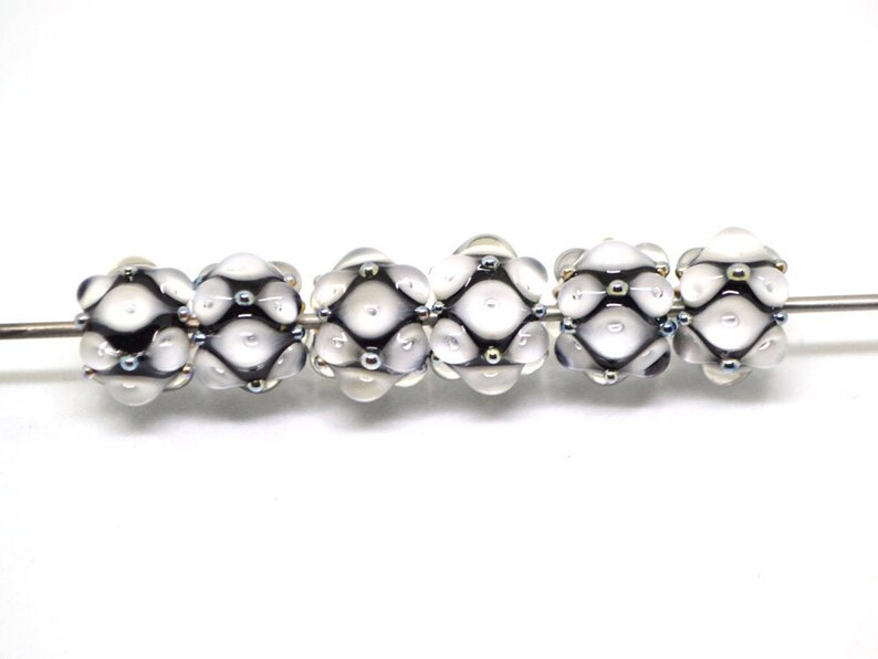 May include: Six white glass beads with a black and silver geometric pattern. The beads are strung on a silver wire.