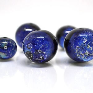 May include: Five blue glass beads with gold and silver flecks. The beads are round and have a speckled appearance.