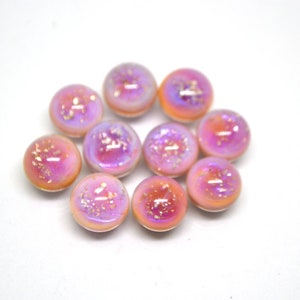 May include: Ten iridescent pink and white glass cabochons with a speckled finish. The cabochons are round and have a smooth, glossy surface.