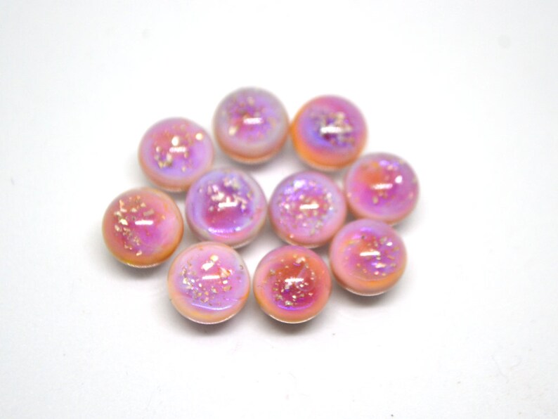 May include: Ten iridescent pink and white glass cabochons with a speckled finish. The cabochons are round and have a smooth, glossy surface.