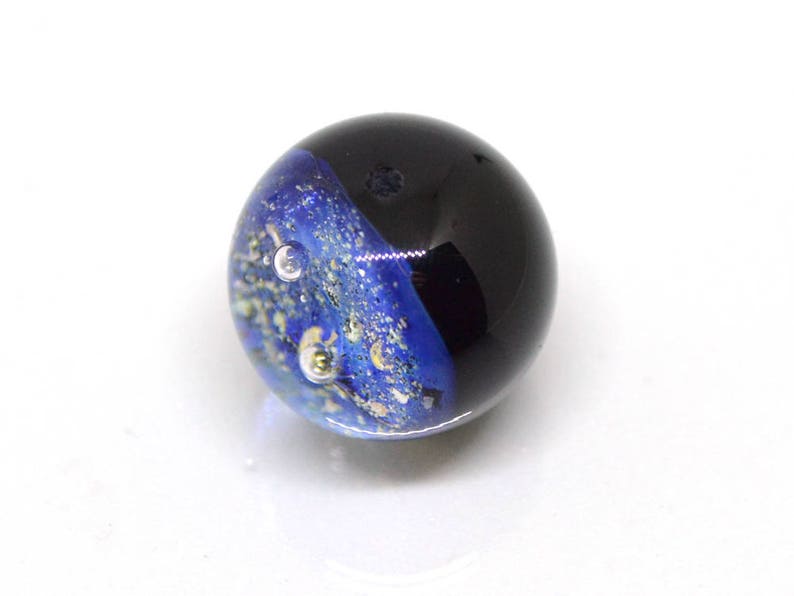May include: A blue and black glass marble with gold flecks and air bubbles. The marble has a swirling pattern.