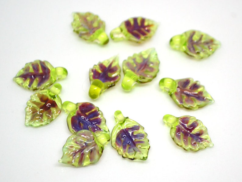May include: A collection of 12 glass leaf charms in shades of green and purple. The leaves have a textured surface and are perfect for adding a touch of nature to jewelry or crafts.