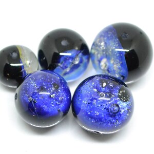 May include: Five glass marbles with blue and black swirling patterns. The marbles have a speckled appearance with small air bubbles trapped inside.