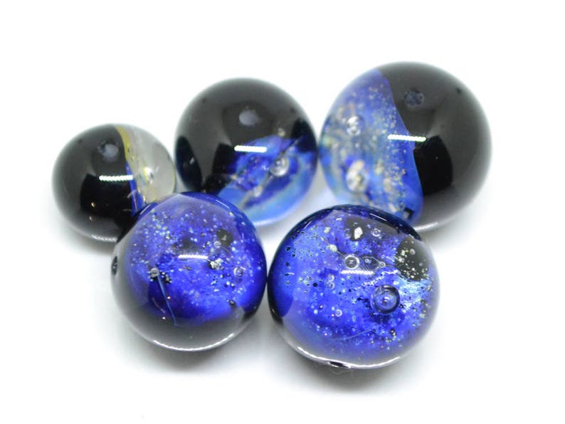 May include: Five glass marbles with blue and black swirling patterns. The marbles have a speckled appearance with small air bubbles trapped inside.