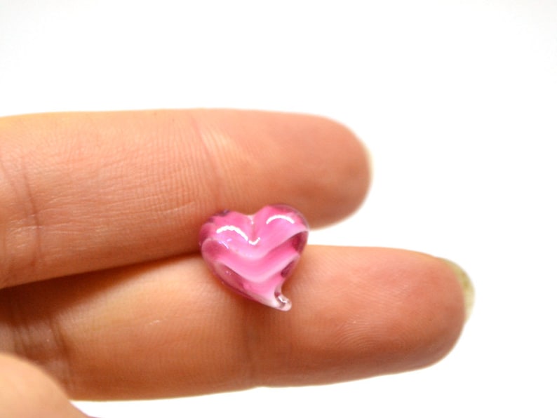 Peut inclure: Un petit c&oelig;ur en verre rose avec un motif en spirale. La perle est petite et a une finition brillante.