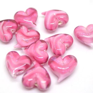 Peut inclure: Un groupe de perles de verre en forme de c&oelig;ur rose et blanc avec un motif en spirale. Les perles sont brillantes et ont une apparence translucide.
