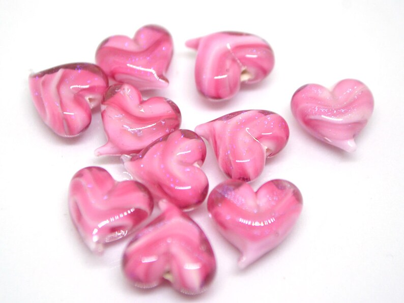 Peut inclure: Un groupe de perles de verre en forme de c&oelig;ur rose et blanc avec un motif en spirale. Les perles sont brillantes et ont une apparence translucide.