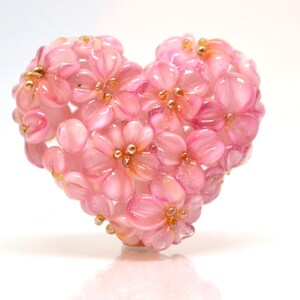 May include: A pink glass heart-shaped ornament made of small pink flowers with gold accents.