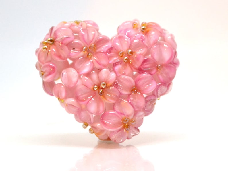 May include: A pink glass heart-shaped ornament made of small pink flowers with gold accents.