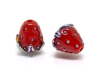 May include: Two red glass strawberry beads with silver accents. The beads are shaped like strawberries with a detailed design.