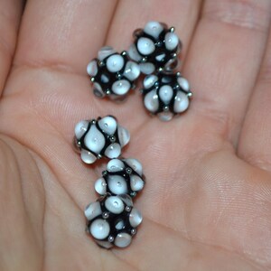 May include: Five white and black glass beads with a textured surface. The beads are round and have a cluster of small white dots on each bead.