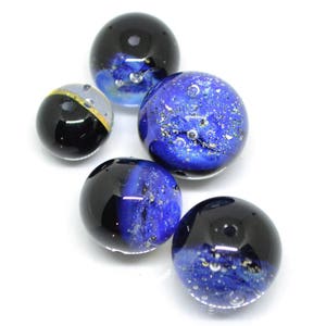 May include: Five glass marbles with blue and black swirling patterns. The marbles have a speckled appearance with air bubbles trapped inside.