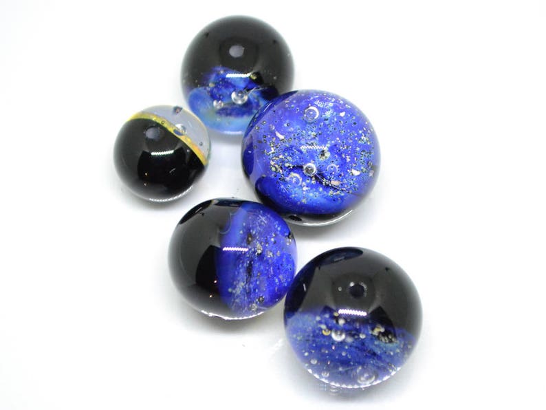 May include: Five glass marbles with blue and black swirling patterns. The marbles have a speckled appearance with air bubbles trapped inside.