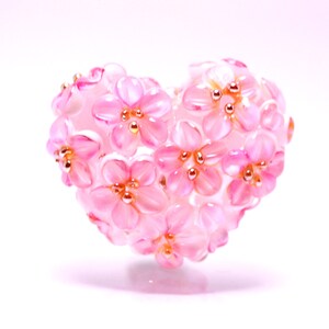 May include: A pink heart-shaped ornament made of small pink flowers with gold centers.