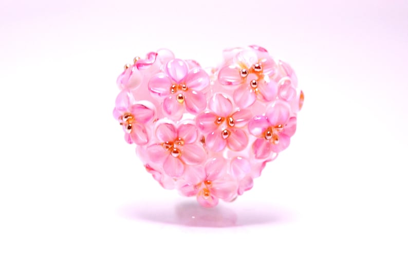 May include: A pink heart-shaped ornament made of small pink flowers with gold centers.