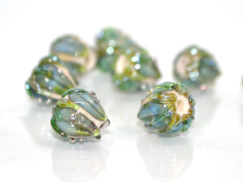 K&ouml;nnte beinhalten: Eine Sammlung gr&uuml;ner, blauer und wei&szlig;er Glasperlen mit aufwendigen Designs. Die Perlen haben eine einzigartige, organische Form und sind perfekt f&uuml;r die Schmuckherstellung.