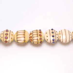 May include: A string of eight round, cream-colored beads with different patterns of brown, gold, and blue accents. The beads are strung on a silver wire.