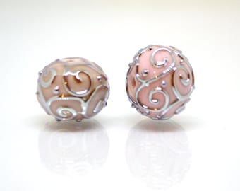 May include: Two pink glass beads with a silver swirl design. The beads are round and have a glossy finish.