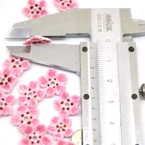May include: Pink ceramic flower beads with a red center, measured with a caliper to be approximately 1.5 cm in diameter.