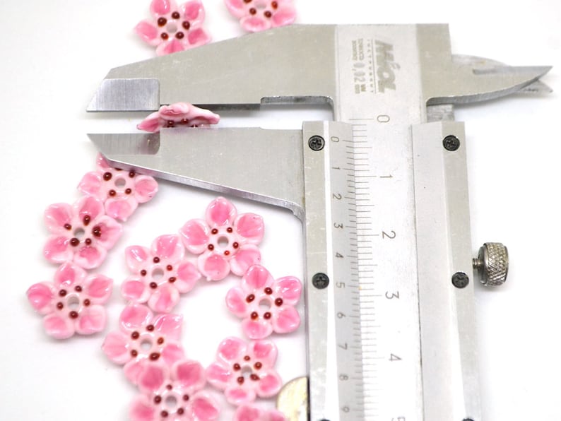 May include: Pink ceramic flower beads with a red center, measured with a caliper to be approximately 1.5 cm in diameter.