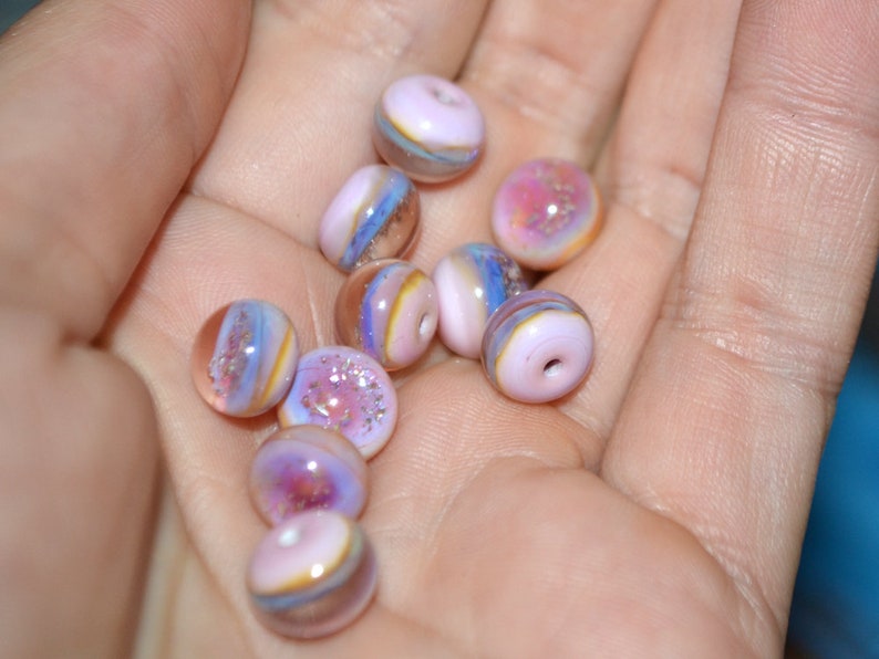 May include: A collection of iridescent glass beads in shades of pink, purple, and blue. The beads have a layered, swirled effect and are perfect for jewelry making.