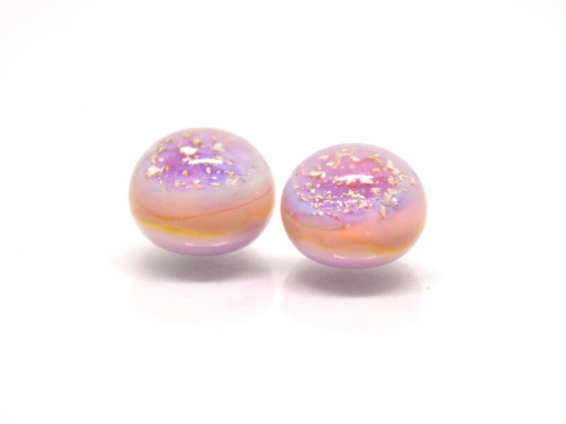 May include: Two round glass beads with a pink and purple iridescent finish. The beads have a subtle shimmer and are speckled with gold glitter.