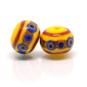 May include: Two yellow glass beads with red and brown stripes and blue and black eye designs.