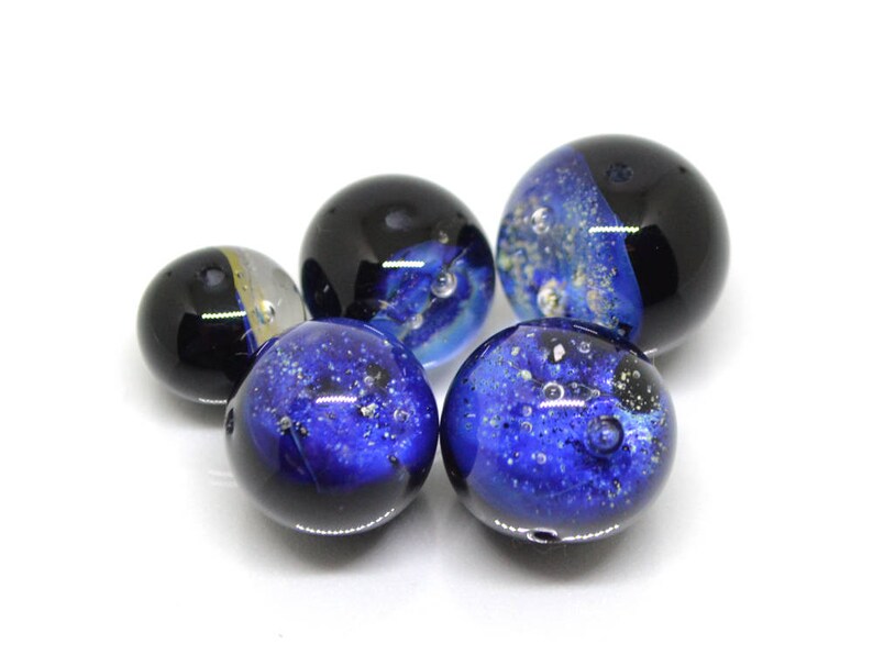 May include: Five glass marbles with blue and black swirling patterns. Some of the marbles have gold flecks.