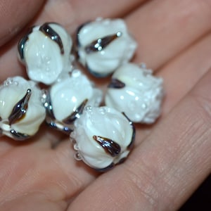 May include: A collection of six white glass beads with black and brown swirls. The beads are round and have a smooth, glossy finish.