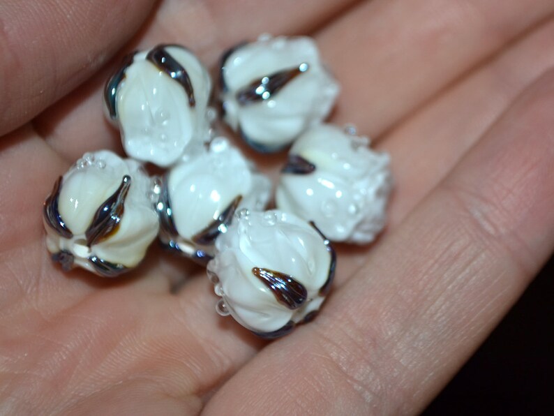 May include: A collection of six white glass beads with black and brown swirls. The beads are round and have a smooth, glossy finish.