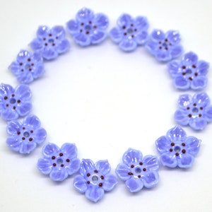May include: A circle of 12 light blue flower-shaped buttons with a dark purple center. The buttons are arranged in a circle on a white background.