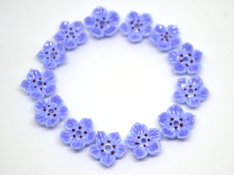 May include: A circle of 12 light blue flower-shaped buttons with a dark purple center. The buttons are arranged in a circle on a white background.