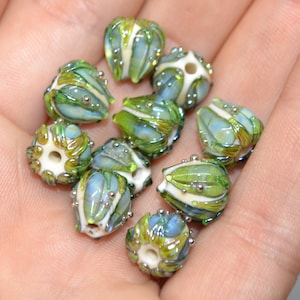 K&ouml;nnte beinhalten: Eine Sammlung von neun gr&uuml;nen und wei&szlig;en Glasperlen mit aufwendigen Designs. Die Perlen haben eine perlmuttartige Oberfl&auml;che und sind mit silbernen Punkten verziert.