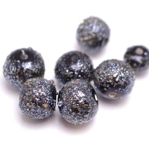 Op de afbeelding: Een groep zwarte en zilveren glitter kralen. De kralen zijn rond en hebben een glanzende afwerking.
