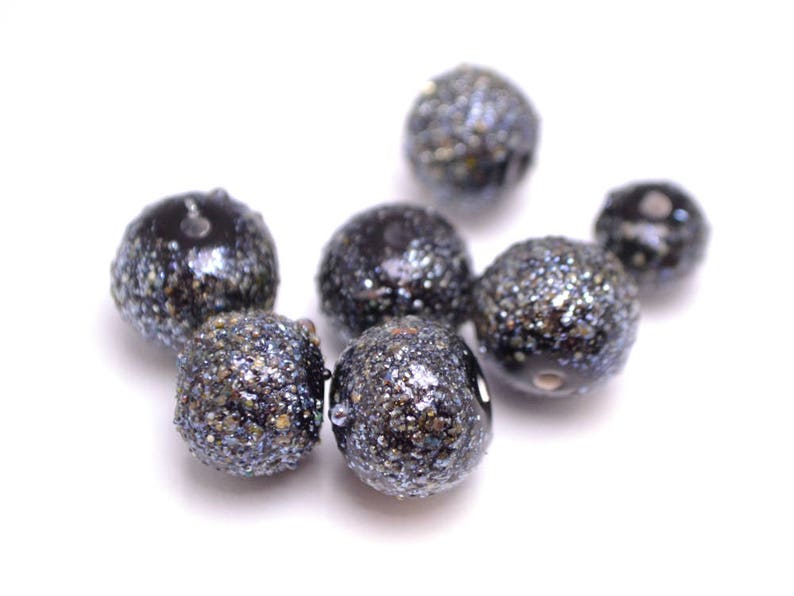 Op de afbeelding: Een groep zwarte en zilveren glitter kralen. De kralen zijn rond en hebben een glanzende afwerking.