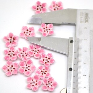 May include: Pink ceramic flower beads with a red center, measured with a ruler. The beads are approximately 1 cm in diameter.