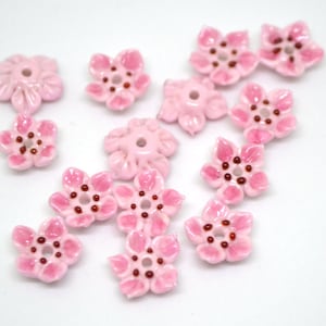 May include: Pink ceramic flower beads with a light pink glaze and dark pink centers. The beads are shaped like five-petal flowers.